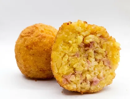 Arancino Cotto e Caciocavallo tagliato a metà, riso giallo con prosciutto cotto, accanto a un arancino intero dorato