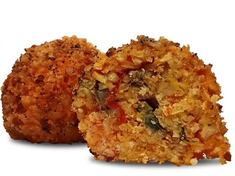 Arancino alla Norma tagliato a metà, ripieno con pomodoro e melanzane, accanto a un arancino intero