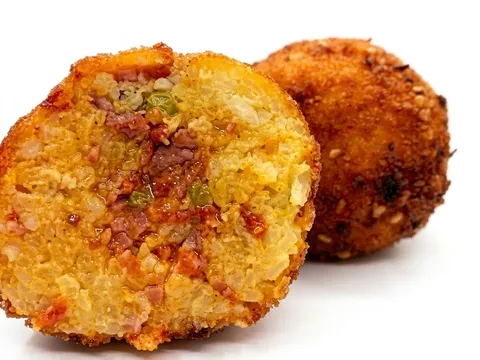 Arancino Ventricina e Provola tagliato a metà, riso allo zafferano con ventricina piccante, accanto a un arancino intero dorato